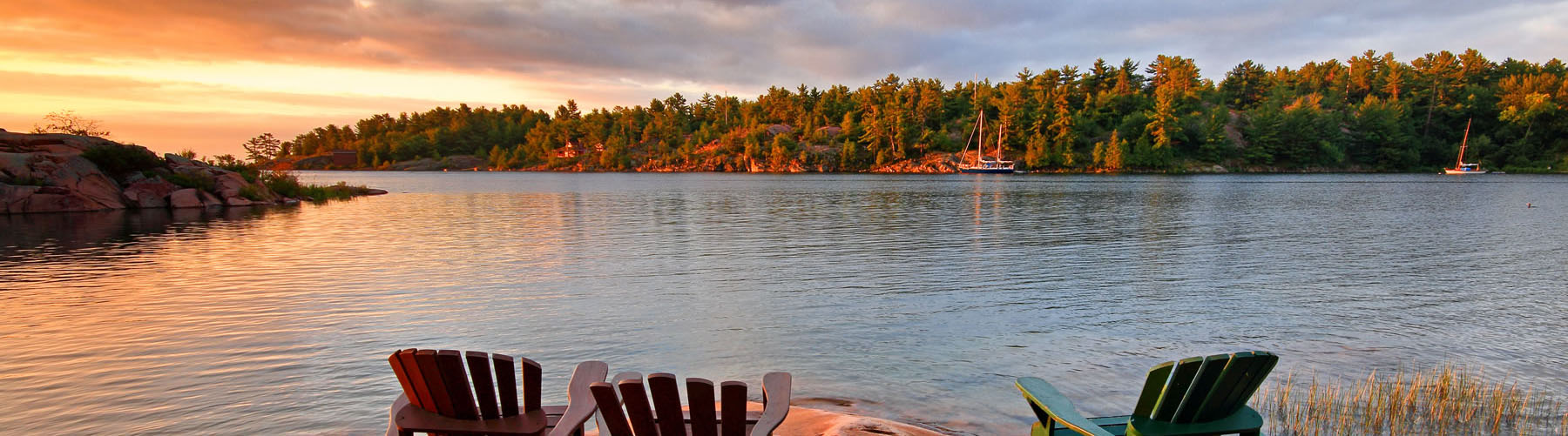 Scenic view of lakefront cottage in the morning with three Muskoka chairs